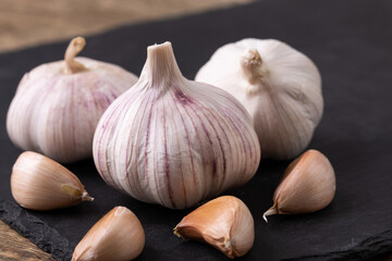 Unpeeled garlic bulb closeup with garlic cloves around it on a black slate 