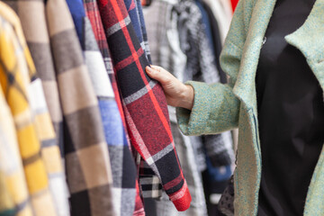 A woman chooses a plaid shirt in a clothing store.