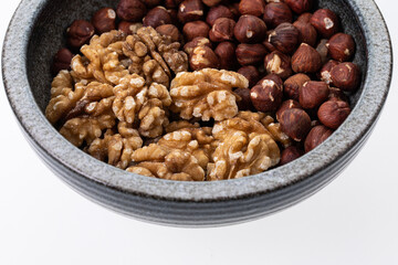 Peeled walnuts and hazelnuts in a grey, handmade bowl on white 