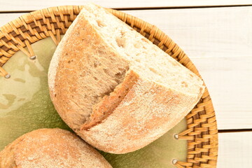 Two halves of a fragrant loaf without yeast with cereal with bran in a ceramic dish, close-up, isolated on a white wooden table.