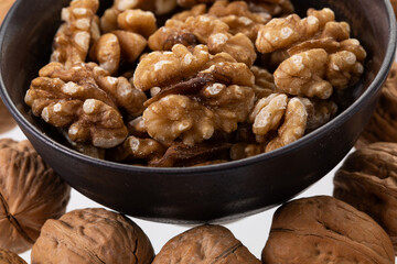 Peeled walnuts in a brown bowl with unpeeled walnuts around it 