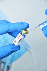 A doctor wearing blue gloves holds a bottle of COVID-19 vaccine.