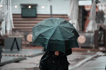 woman walking in the city with green umbrella on rainy and windy day.