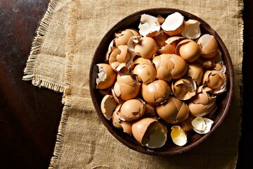 Egg shells in a bowl on hessian cloth on a wooden table.