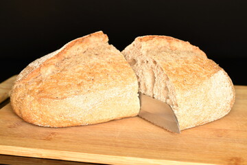 Two halves of a fragrant loaf without yeast with bran flakes on a bamboo board, close-up, isolated on black.