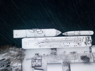 Snow-covered barges in the industrial port. Snowy day, blizzard. Aerial drone view.