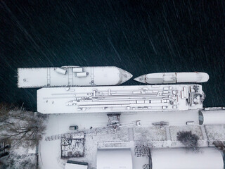 Snow-covered barges in the industrial port. Snowy day, blizzard. Aerial drone view.