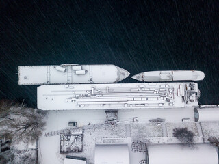 Snow-covered barges in the industrial port. Snowy day, blizzard. Aerial drone view.
