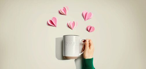 Female hand holding a mug with paper craft hearts - flat lay