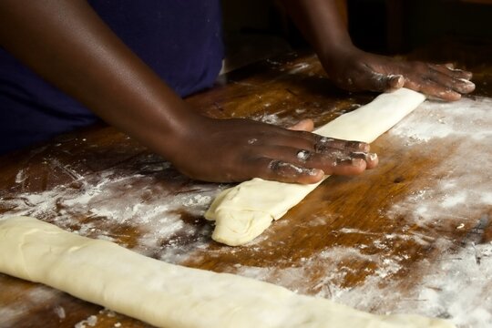 black persons hands folding pastry on a flour dusted wooden table