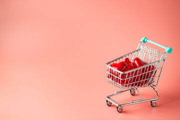 Shopping cart full of hearts for Valentine's Day on pink background