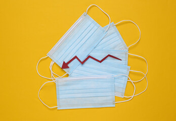 Facial medical masks and a falling arrow on yellow background. Decrease in covid-19 infection statistics