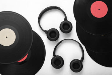 Two pairs of black stereo headphones and vinyl records on white background