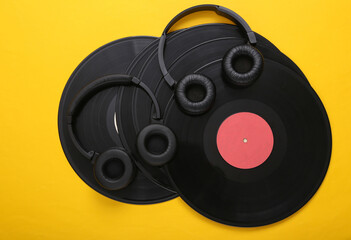 Two pairs of black stereo headphones and vinyl records on yellow background