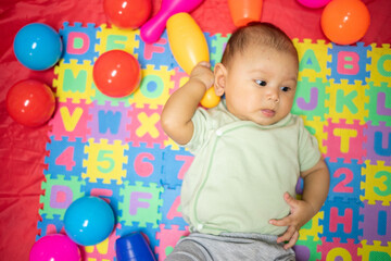 Fototapeta na wymiar 3-4 Month Old Baby GIrl lying on play mat playing with colored toys developing her eyes and motor skills, young baby girl grasping and holding her toys