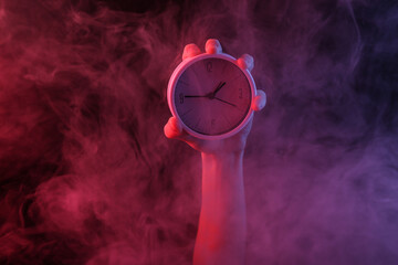 Hand holding clock in dense smoke with red-blue neon light.