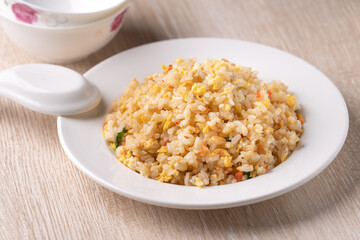 Chinese fried rice in white plate on bright wooden table background.