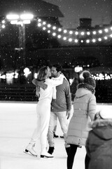 Happy couple of lovers having fun, hugging an kissing at ice skating rink outdoor. St. Valentines Day, Winter leisure, New Year holidays concept.