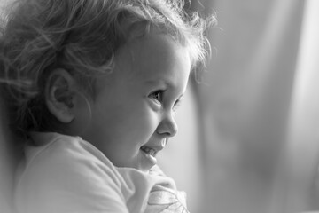 Close up of a cute fair haired child smiling fascinatingly and looking at something in front of her. Beige background, portrait, social issues, copy space