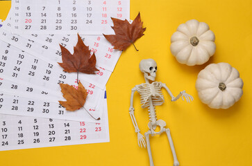 Halloween theme. Skeleton with pumpkins, fallen leaves and a calendar on a yellow background. Top view