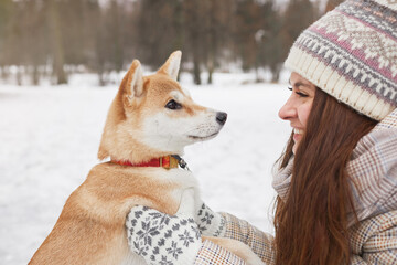 Side view portrait of smiling young woman holding cute dog while enjoying walk together outdoors in winter