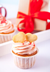 Valentines cupcakes cream cheese frosting decorated with heart shaped cookies and gift box on the background.