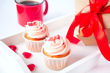 Valentines cupcake cream cheese frosting decorated with heart candy, mug of coffee and gift box on the background.