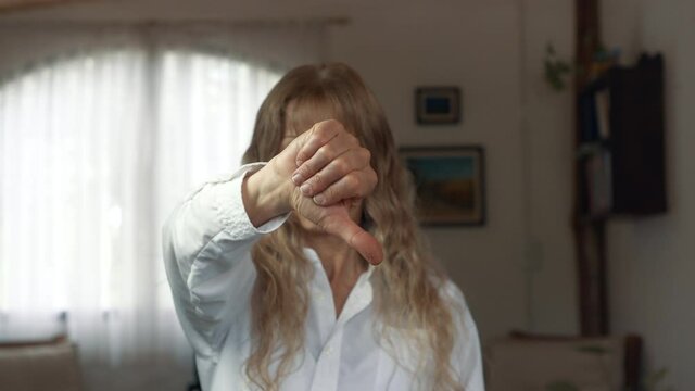 Blond woman pointing her thumb down in her living room. Steady close up shot