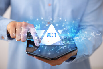 Businessman holding a foldable smartphone with AUDIT inscription, business concept