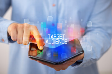 Young man holding a foldable smartphone with TARGET AUDIENCE inscription, educational concept