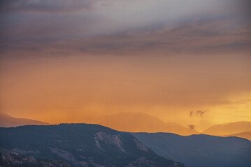 Atmospheric landscape with silhouettes of mountains and forest on rock on background of vivid orange dawn sky. Colorful nature scenery with sunset or sunrise of illuminating color. Sundown paysage.