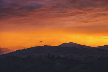 Atmospheric landscape with silhouettes of mountains with trees on background of vivid orange pink violet dawn sky. Colorful nature scenery with sunset or sunrise of illuminating color. Sundown paysage