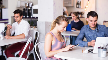 Young woman with boyfriend busying with device during meeting in modern cafe