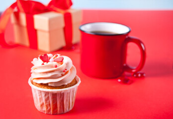 Valentines cupcake cream cheese frosting decorated with heart candy, mug of coffee and gift box on the red background.