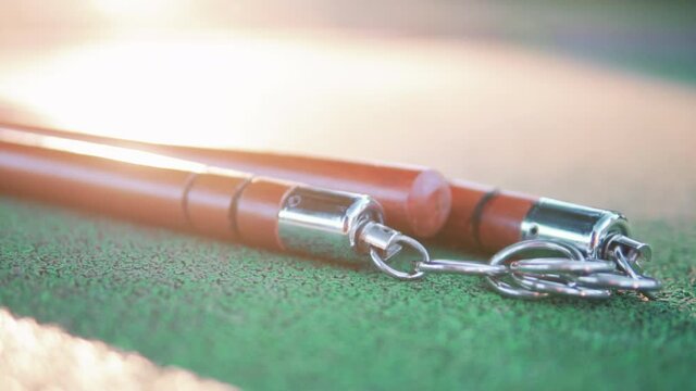 Red Wooden Nunchucks With Metal Chain Lies On Floor. - closeup
