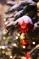 A red Christmas ball hangs on a pine tree against the backdrop of a city landscape. Close-up of a large red Christmas trinket on the Christmas tree.
