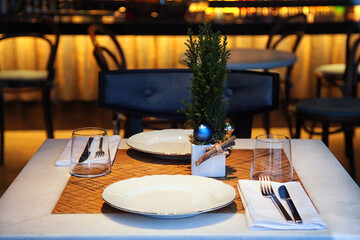 Christmas table in the cafe, white plates, wooden chairs.