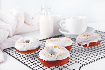 Doughnuts on the baking rack glazed white chocolate cream or icing and bottle with milk on the background.