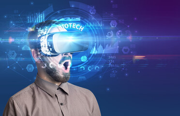 Businessman looking through Virtual Reality glasses with BIOTECH inscription, innovative technology concept