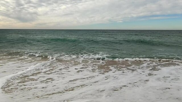 Smooth pan shot during walk along golden beach shore with crashing waves during beautiful summer day.