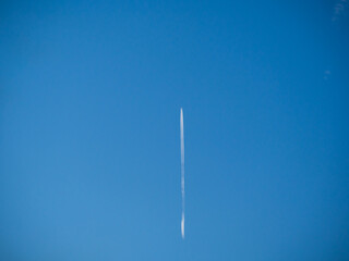 Clear blue sky, divided in half by the white double track of a flying jet.