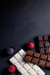 Three types of chocolate - black, milk and white with luxury handmade chocolates on a black background with copy space