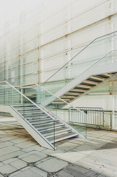 Escalera urbana blanca en perspectiva diagonal, construida en acero, con barandillas tubulares y cristales azulados