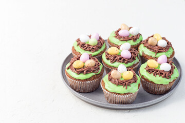 Carrot cupcakes with cream cheese frosting and Easter chocolate eggs, on gray plate, horizontal, copy space