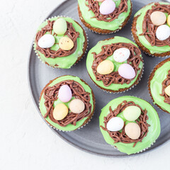 Carrot cupcakes with cream cheese frosting and Easter chocolate eggs, on a gray plate, top view, square