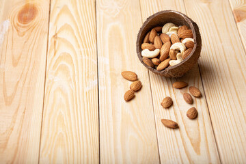 Mix of almonds, cashew nuts in coconut bowl on wood table copy space. Vegan protein source
