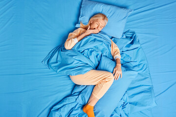 Top view of blonde forty years old European woman awakes early in morning yawns and covers mouth...