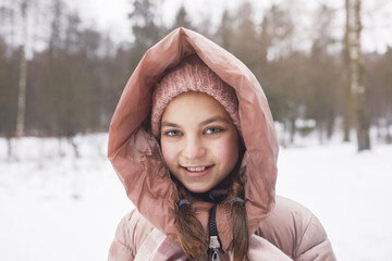 Front view portrait of cute girl wearing pink jacket and smiling at camera while enjoying walk outdoors in winter, copy space