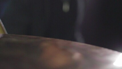 Smooth close up of a drum crash cymbal being hit with a stick. Cymbal wobbling afterwards. Dark Background. Super slow motion. Dolly Gimbal forward movement. Shallow depth with fixed focus.	