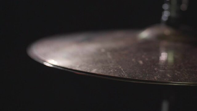 Smooth close up of a drum hi-hat being played with sticks. Super Close up with a dark background. Gimbal panning movement. Shallow depth with fixed focus. Shot in 4K.	